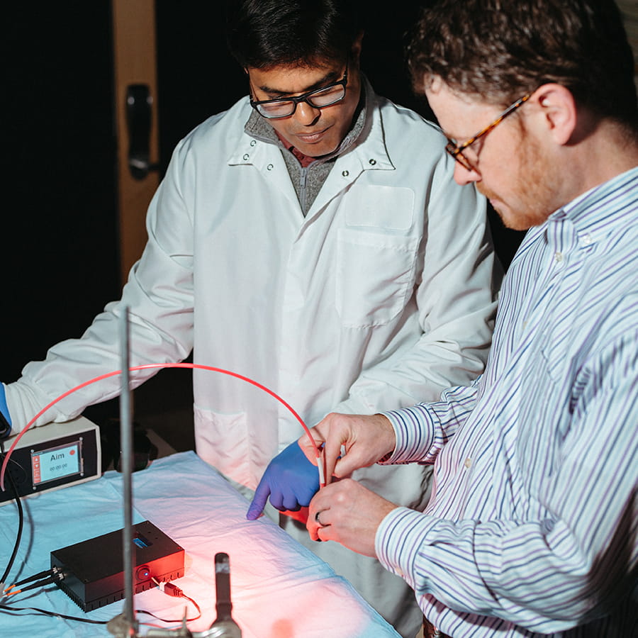 Two researchers work in lab on a tool that has a light.