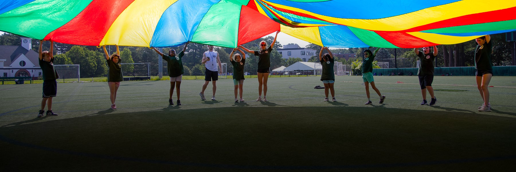 students in long line holding colorful rainbow banner above heads