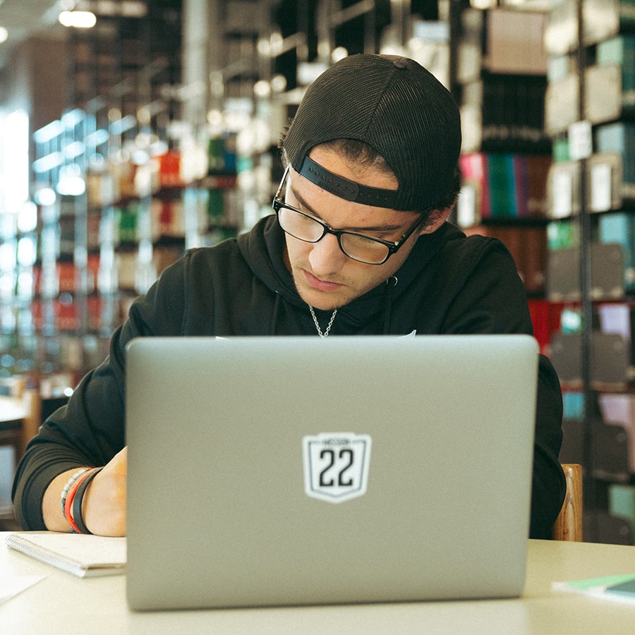 Male student at laptop in library with books in background.