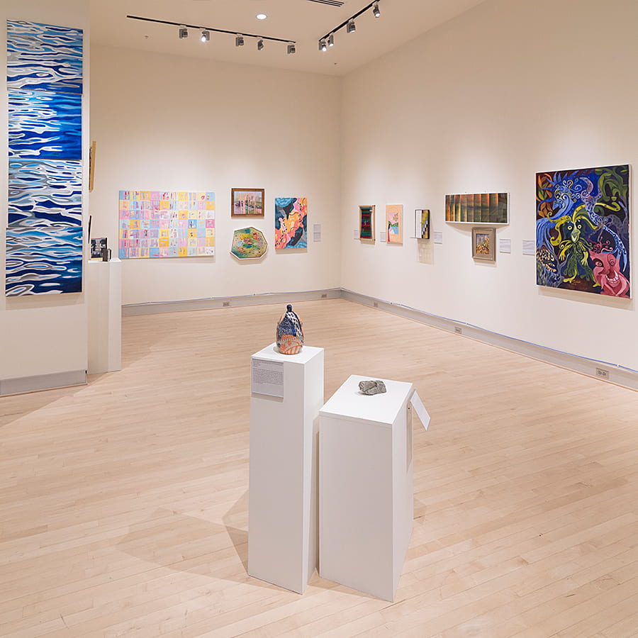 People in university hall gallery gather around a speaker in front of the art.